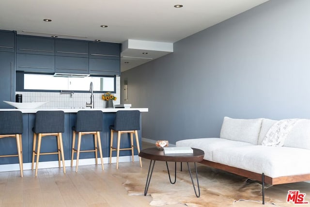 kitchen with a kitchen breakfast bar, light hardwood / wood-style flooring, blue cabinets, kitchen peninsula, and decorative backsplash