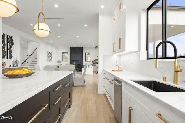 kitchen featuring pendant lighting, light stone counters, white cabinetry, and sink