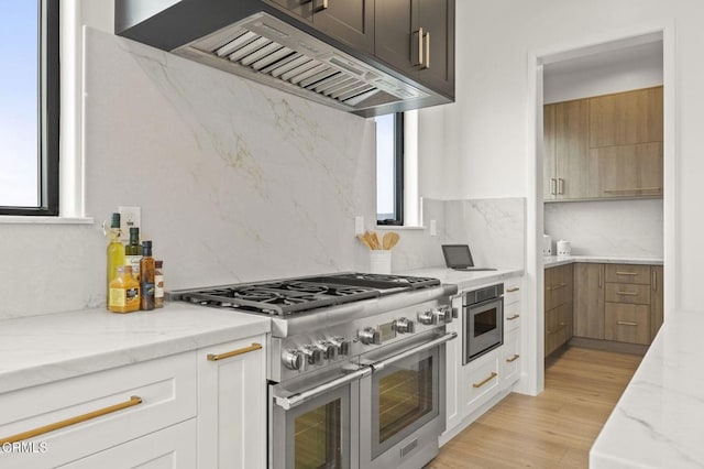 kitchen with white cabinetry, stainless steel appliances, light stone counters, light hardwood / wood-style flooring, and ventilation hood