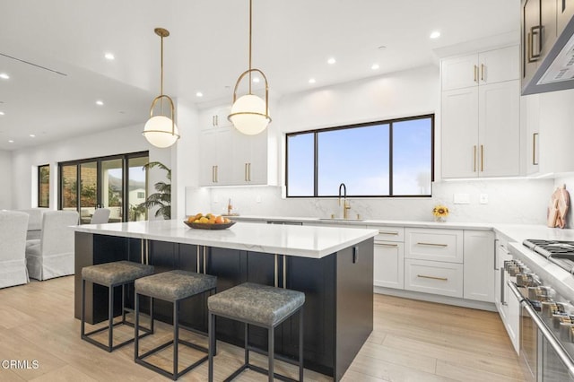 kitchen featuring white cabinets, decorative light fixtures, light wood-type flooring, and high end stainless steel range oven