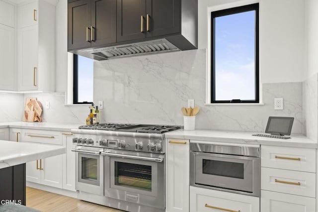 kitchen featuring backsplash, light stone countertops, light wood-type flooring, appliances with stainless steel finishes, and white cabinetry