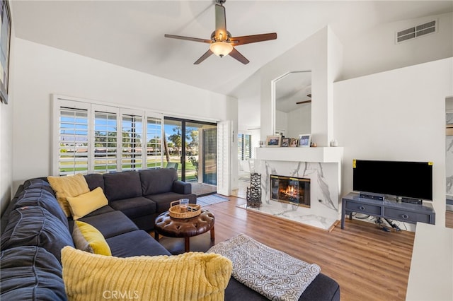 living room with visible vents, a ceiling fan, a high end fireplace, wood finished floors, and high vaulted ceiling