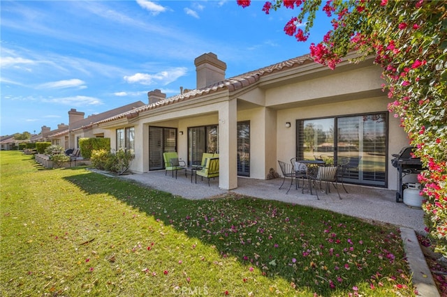 back of property featuring a chimney, a patio, a lawn, and stucco siding