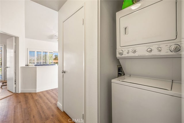 laundry room with baseboards, light wood-style flooring, and stacked washing maching and dryer