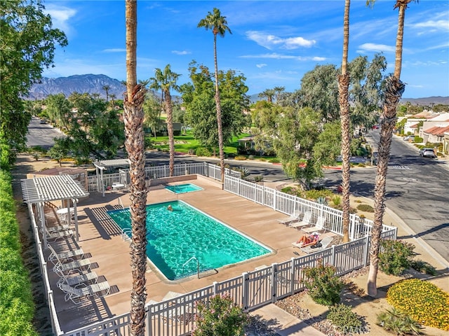 community pool featuring a patio area, a mountain view, and fence