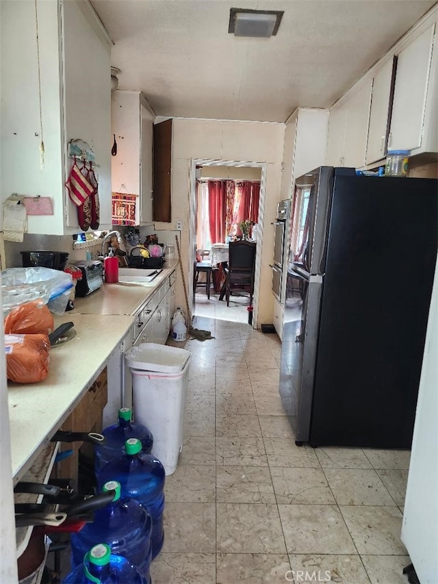 kitchen with black refrigerator, white cabinets, and sink