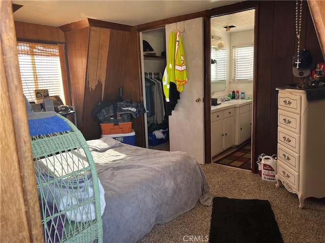 carpeted bedroom featuring ensuite bathroom, a closet, and wooden walls