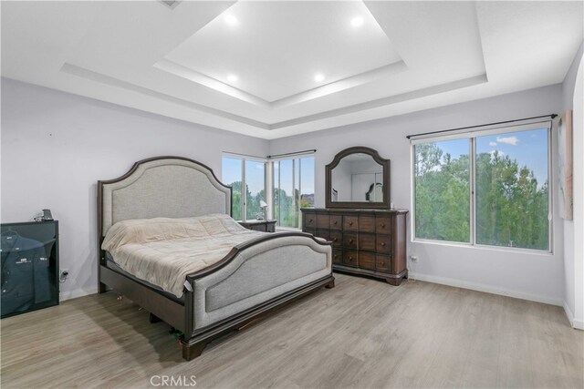 bedroom featuring a tray ceiling, multiple windows, and light wood-type flooring