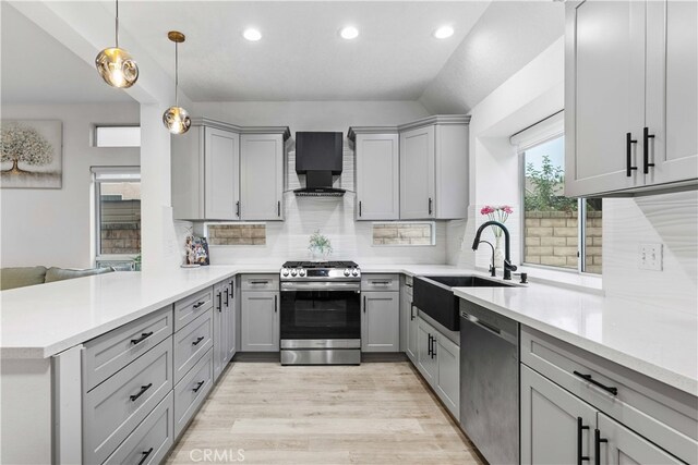 kitchen featuring wall chimney range hood, gray cabinets, appliances with stainless steel finishes, decorative light fixtures, and kitchen peninsula