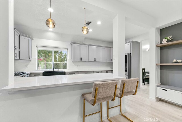 kitchen featuring a kitchen breakfast bar, kitchen peninsula, light hardwood / wood-style flooring, and hanging light fixtures