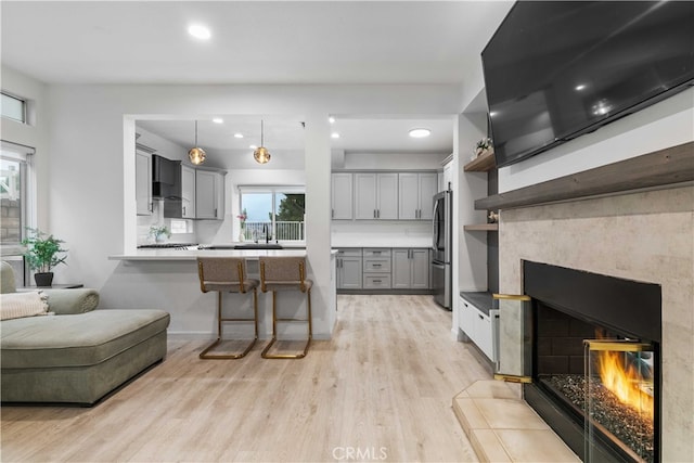 kitchen featuring gray cabinetry, pendant lighting, light hardwood / wood-style flooring, a fireplace, and stainless steel refrigerator