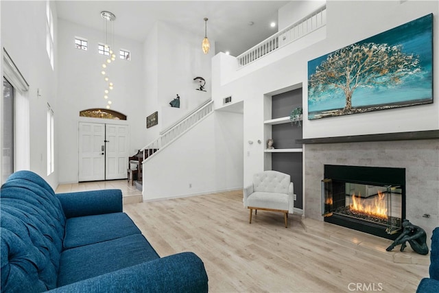 living room with built in shelves, a towering ceiling, and light wood-type flooring