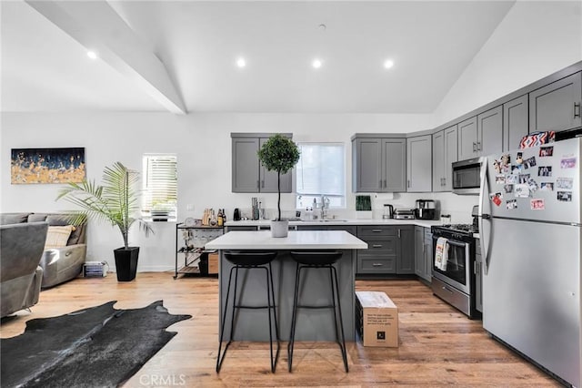 kitchen with vaulted ceiling, a kitchen island, sink, a breakfast bar area, and stainless steel appliances