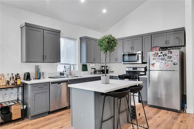 kitchen featuring lofted ceiling, sink, gray cabinetry, a center island, and stainless steel appliances