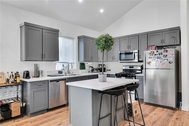 kitchen featuring lofted ceiling, sink, appliances with stainless steel finishes, gray cabinetry, and a kitchen island