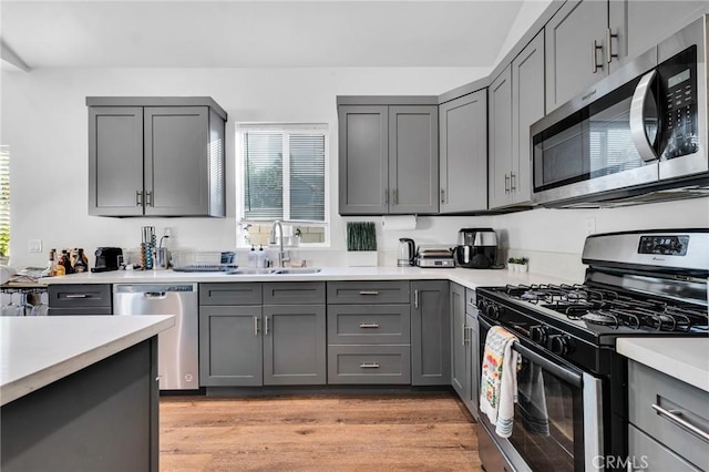 kitchen with gray cabinets, appliances with stainless steel finishes, sink, and light hardwood / wood-style flooring