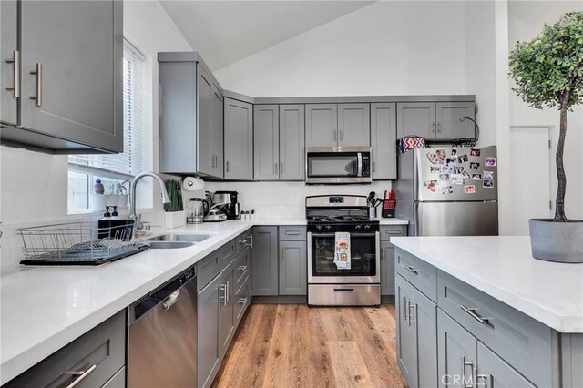 kitchen with sink, appliances with stainless steel finishes, gray cabinetry, light hardwood / wood-style floors, and vaulted ceiling