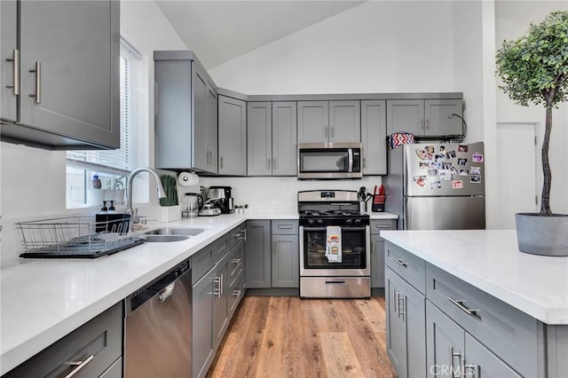 kitchen with lofted ceiling, sink, gray cabinetry, stainless steel appliances, and light wood-type flooring