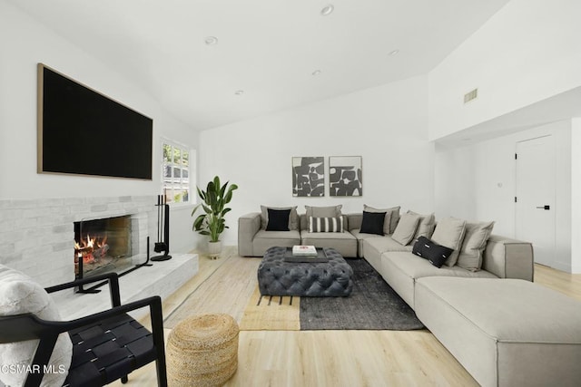 living room with vaulted ceiling, a fireplace, and light hardwood / wood-style floors