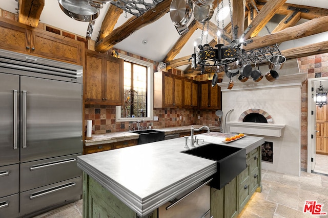 kitchen featuring stainless steel built in fridge, sink, a center island with sink, and vaulted ceiling with beams