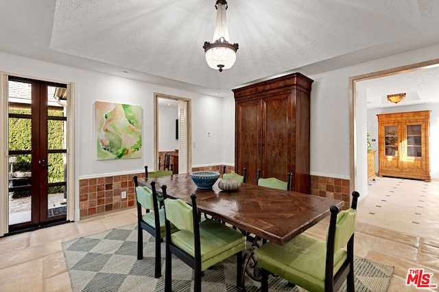 dining area featuring a raised ceiling, a textured ceiling, and french doors