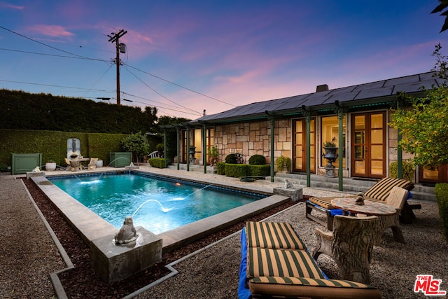 pool at dusk with pool water feature, a patio, and french doors