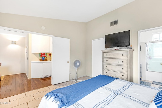 bedroom with ensuite bathroom, lofted ceiling, and light hardwood / wood-style flooring