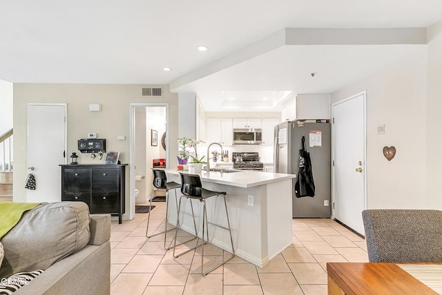 kitchen with sink, a breakfast bar area, light tile patterned floors, white cabinetry, and stainless steel appliances