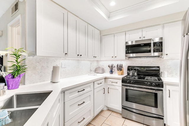 kitchen with white cabinets, a raised ceiling, ornamental molding, light tile patterned floors, and stainless steel appliances