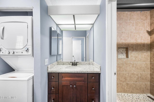 bathroom with stacked washer / dryer, vanity, and tiled shower