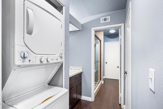 washroom featuring a textured ceiling, stacked washer / drying machine, and dark wood-type flooring