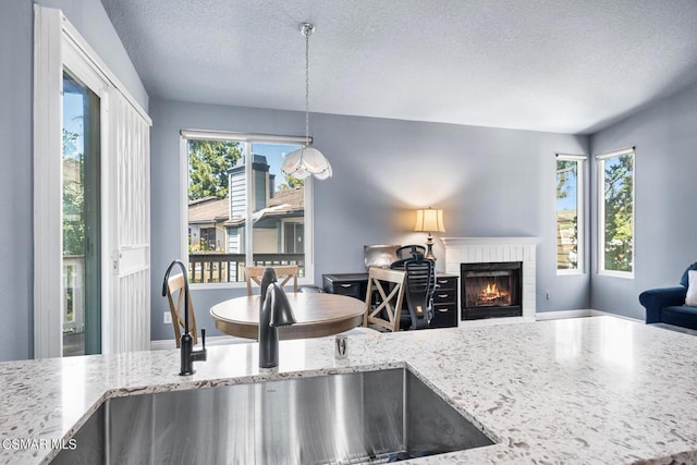 kitchen featuring light stone countertops, sink, hanging light fixtures, a textured ceiling, and a fireplace