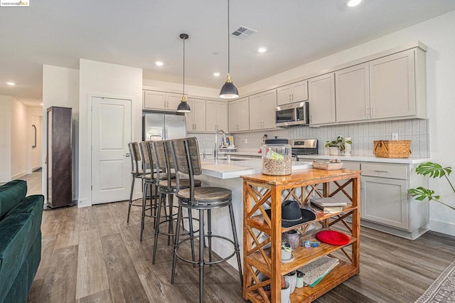 kitchen with pendant lighting, stainless steel appliances, sink, a kitchen island with sink, and hardwood / wood-style flooring