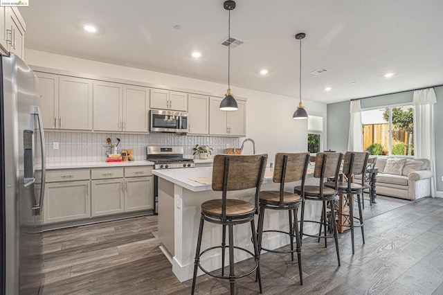 kitchen featuring appliances with stainless steel finishes, decorative light fixtures, dark hardwood / wood-style flooring, an island with sink, and a kitchen breakfast bar