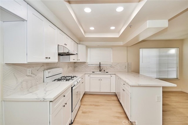 kitchen with kitchen peninsula, light stone counters, white range with gas cooktop, sink, and white cabinets