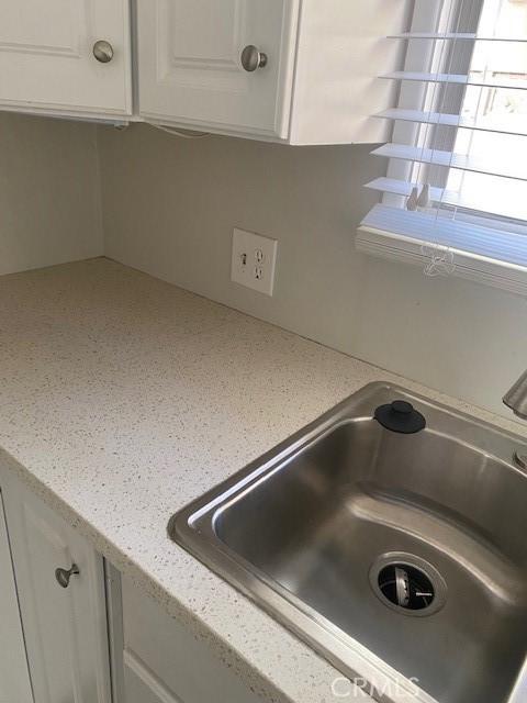 room details featuring white cabinets, light stone counters, and sink