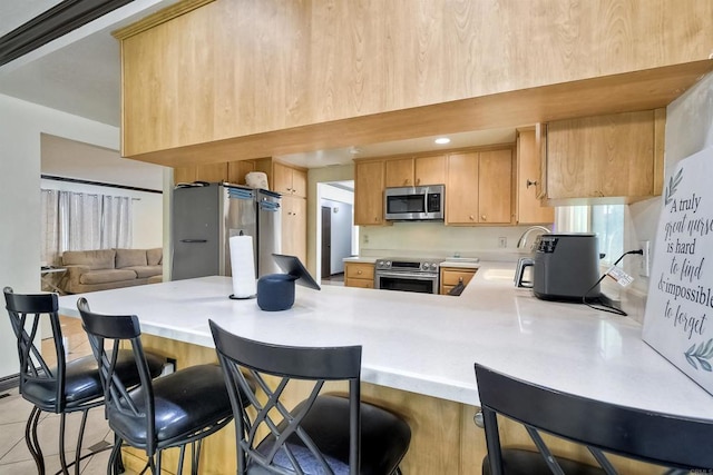 kitchen featuring kitchen peninsula, appliances with stainless steel finishes, a kitchen bar, and light brown cabinetry