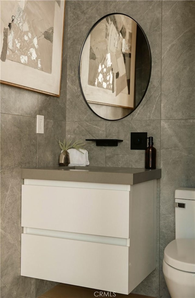 bathroom with vanity, tile walls, and toilet