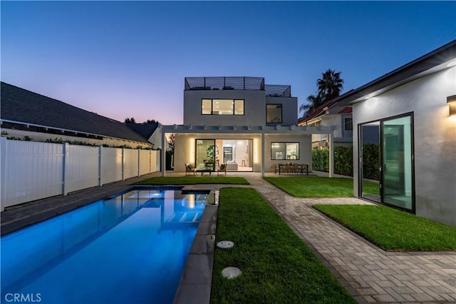 back house at dusk featuring a lawn and a fenced in pool