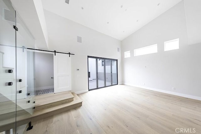 unfurnished room with a barn door, light hardwood / wood-style floors, and high vaulted ceiling