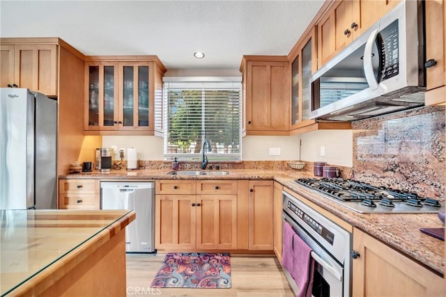 kitchen with light stone counters, sink, stainless steel appliances, and light hardwood / wood-style flooring