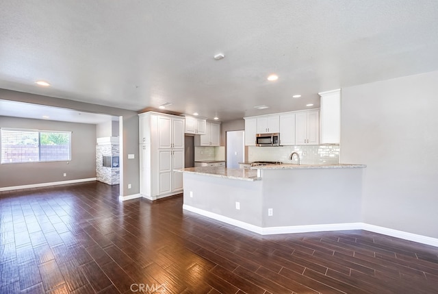 kitchen featuring kitchen peninsula, light stone countertops, backsplash, dark hardwood / wood-style flooring, and white cabinetry