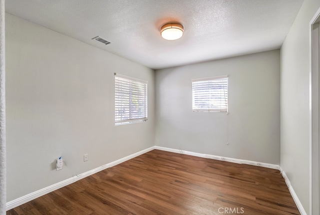 empty room with wood-type flooring, a textured ceiling, and a healthy amount of sunlight
