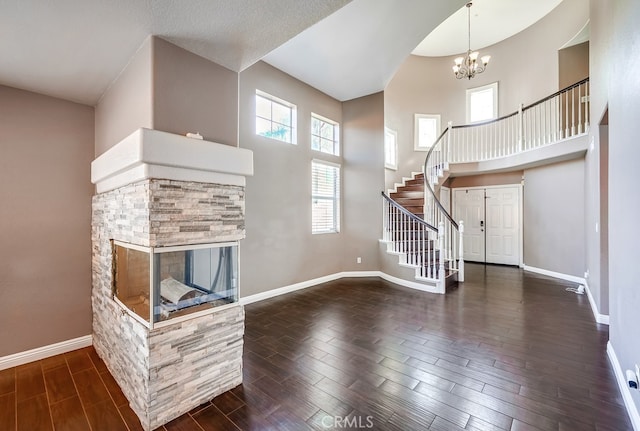 unfurnished living room featuring a stone fireplace, a towering ceiling, and a chandelier