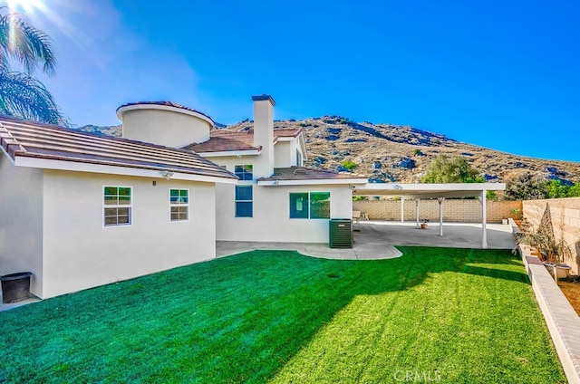 rear view of house with a lawn, central AC, a mountain view, and a patio area