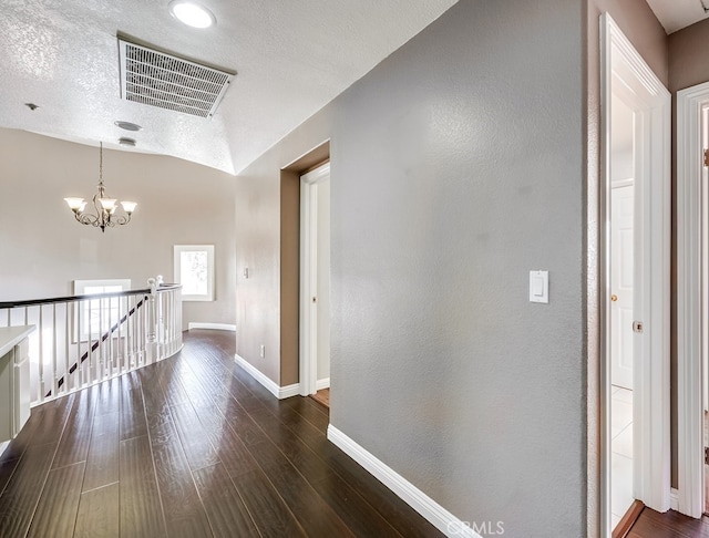 hallway with a notable chandelier, dark wood-type flooring, vaulted ceiling, and a textured ceiling
