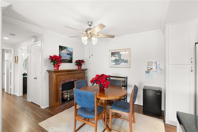 dining space with ceiling fan, dark hardwood / wood-style floors, crown molding, and a fireplace