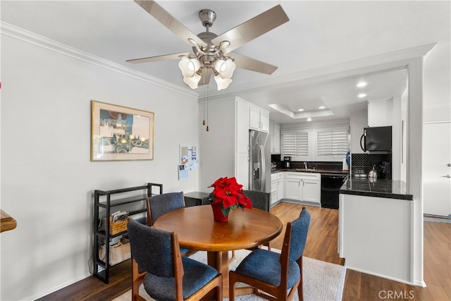 dining area featuring ceiling fan, wood-type flooring, crown molding, and a raised ceiling