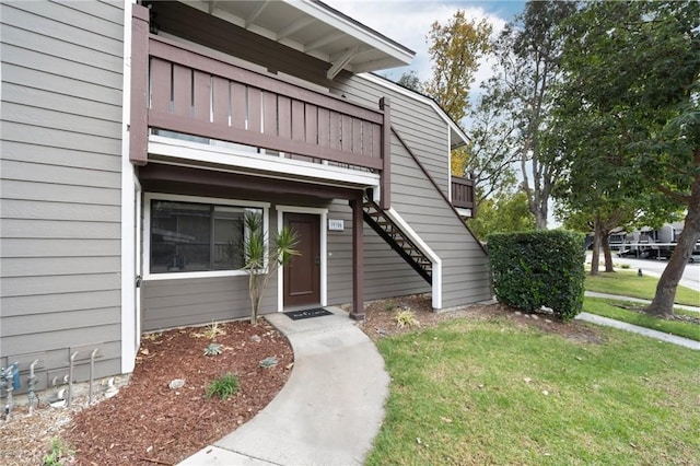 view of exterior entry with a lawn and a balcony