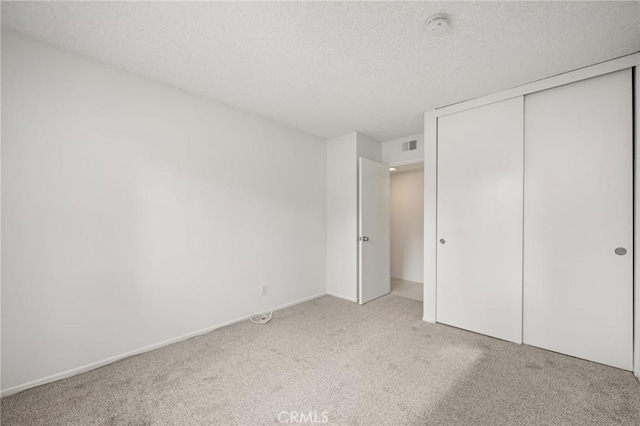 unfurnished bedroom featuring light carpet, a textured ceiling, and a closet